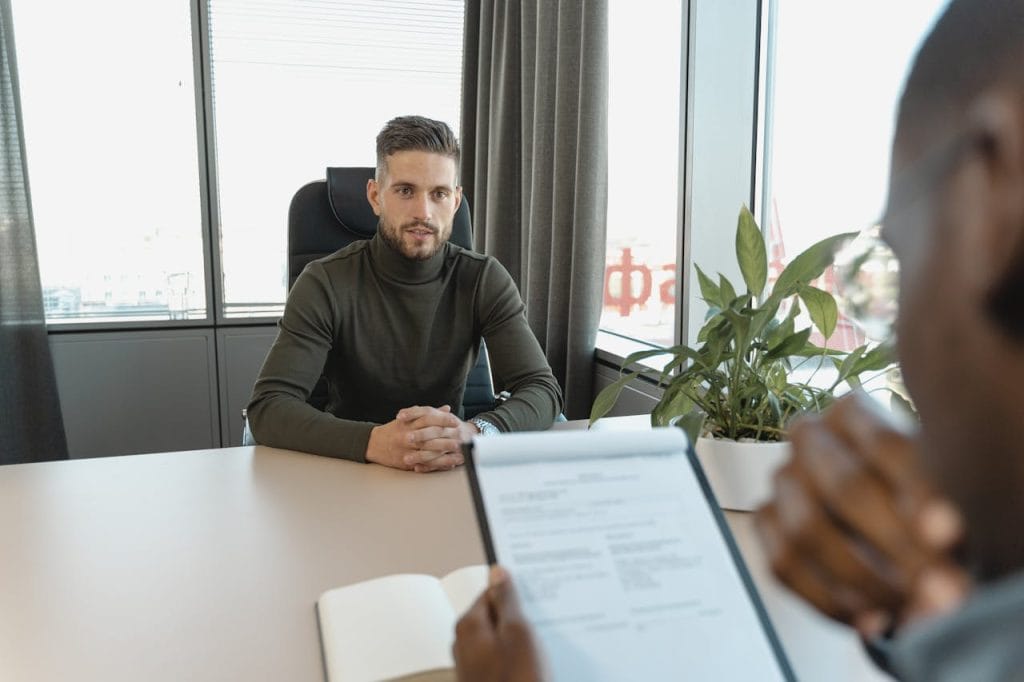 pexels-photo-5439379 Professional man in turtleneck at office desk during an interview.